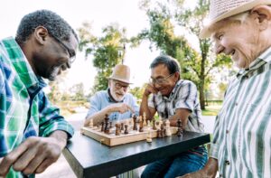 A group of senior friends work on their chess strategies together in a public park on a beautiful, sunny day