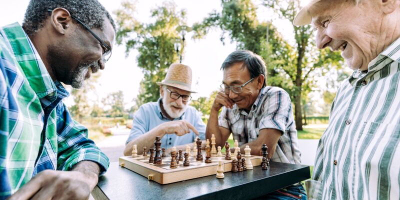 A group of senior friends work on their chess strategies together in a public park on a beautiful, sunny day