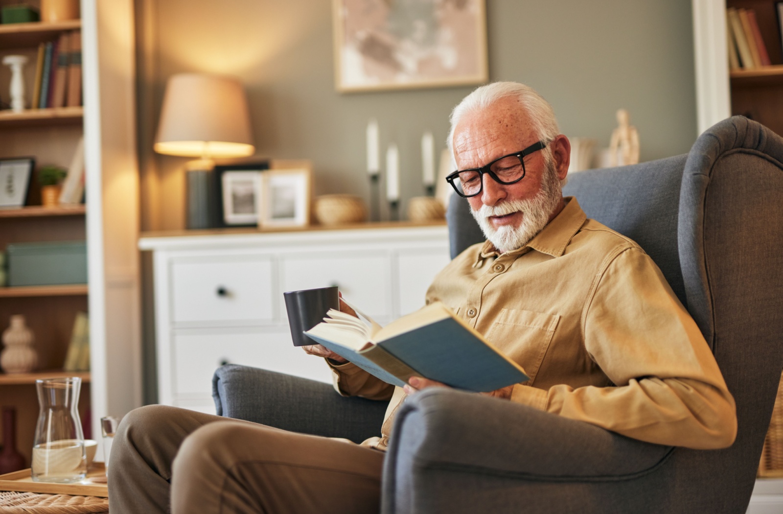 A senior reads a novel while sitting in an armchair in a senior living community