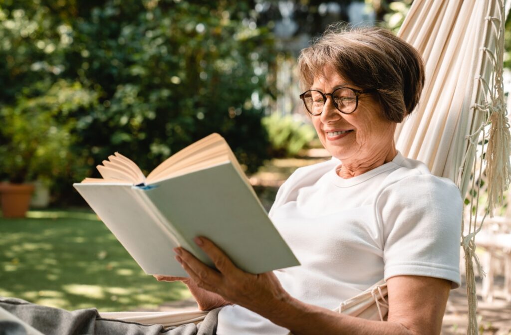 A senior reads a hardcover novel while lounging outside in a hammock.

