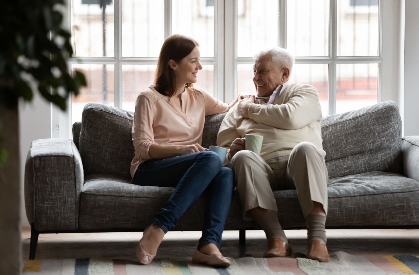 A young adult has a conversation with their senior loved one while sitting on a gray sofa.

