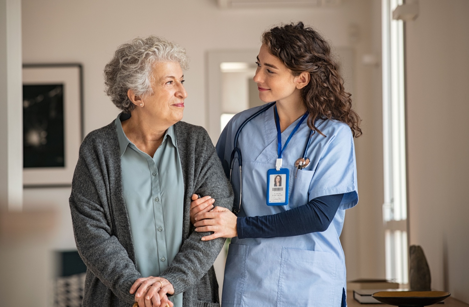 A trained caregiver smiles and holds the arm of a senior memory care resident.