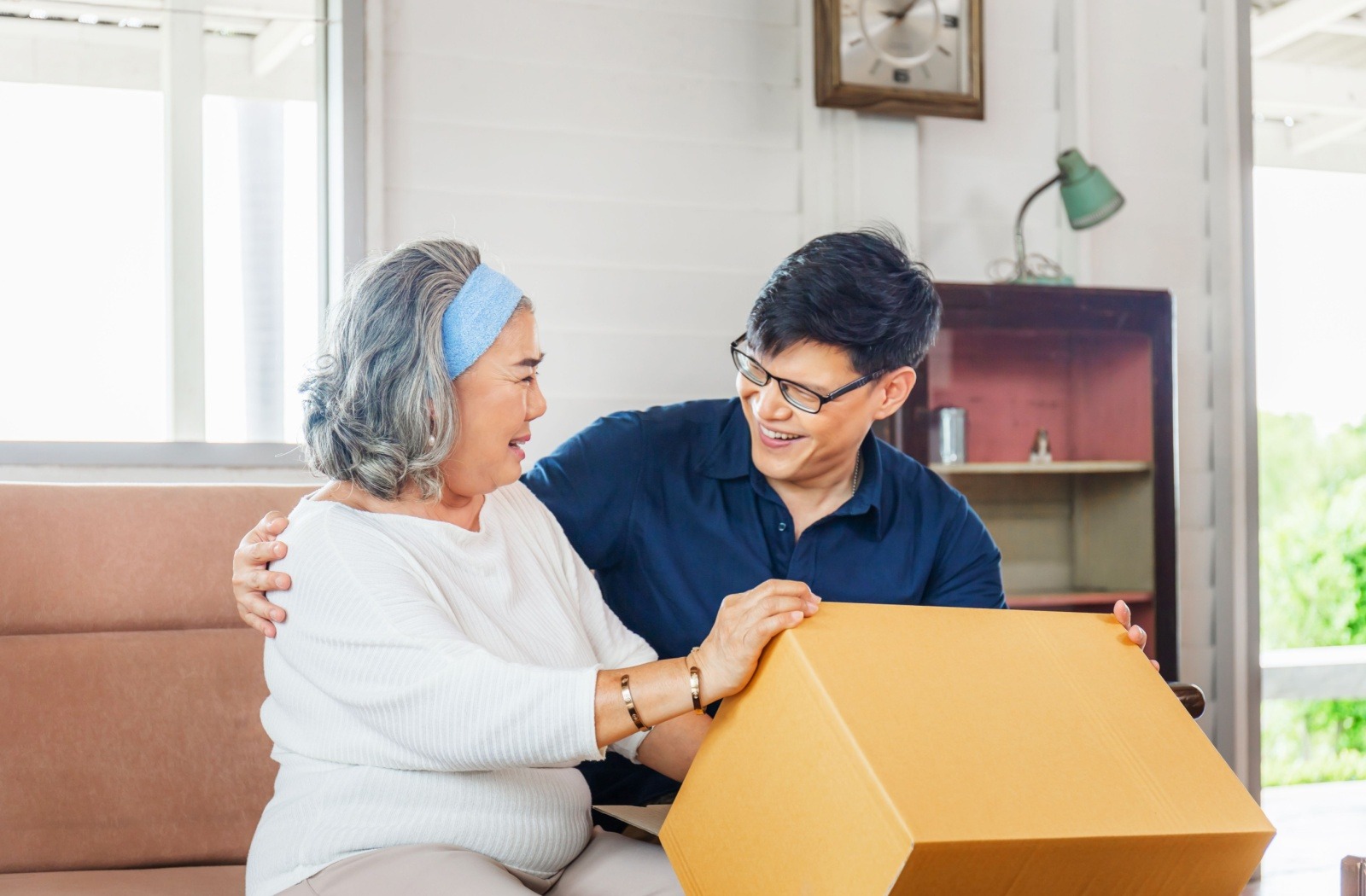 A senior unpacks boxes while moving into their new senior living apartment, with the help of their adult child.