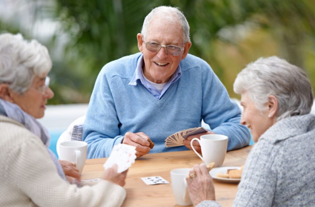 A group of senior friends play a game of cards at an outdoor table at an assisted living community.