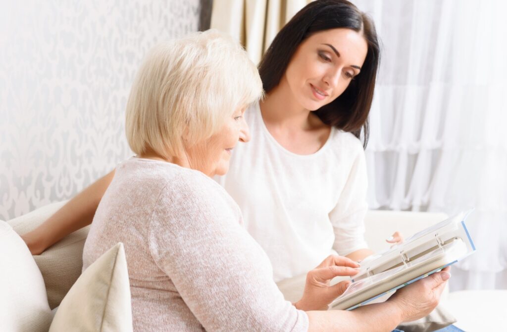 A senior resident and their adult grandchild flip through a family photo album together.