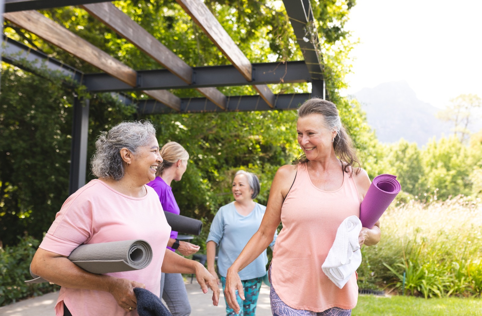 A group of 4 seniors walking with yoga mats and smiling at each other while having conversations.