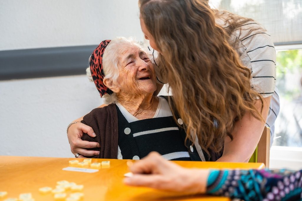 Senior woman laughing with caregiver in the nursing home while playing board skill game